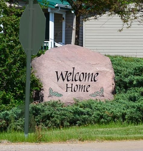 A rock with the phrase "Welcome Home" in a green and grassy community.